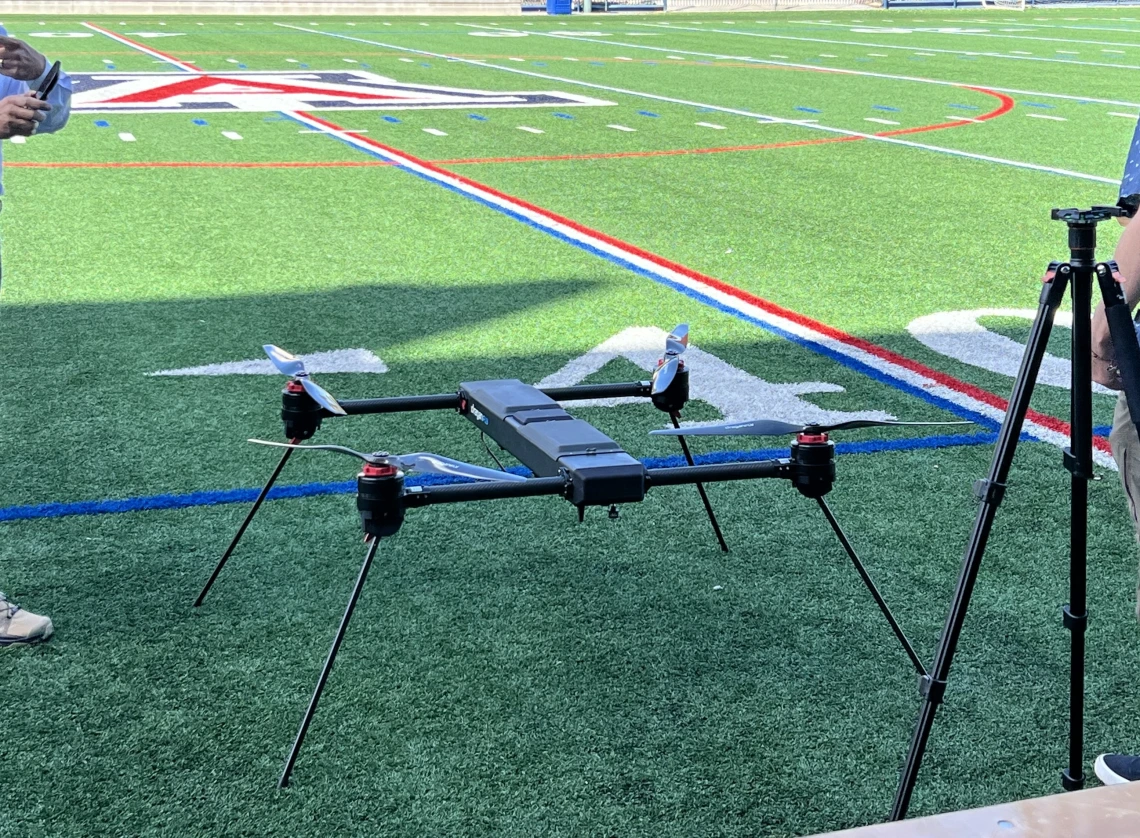 Image of a medium sized drone on a green turf field with the University of Arizona A logo in the background